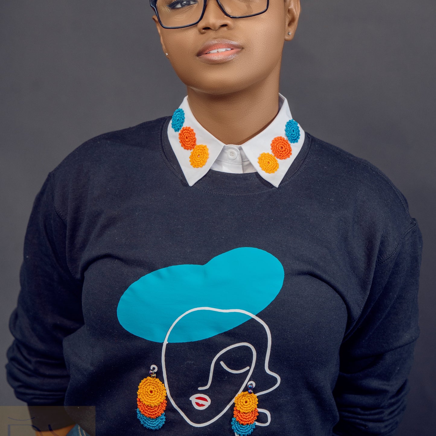 A sweatshirt with a detachable collar featuring a black and white face outline with a blue hat and colorful earrings on the front.
